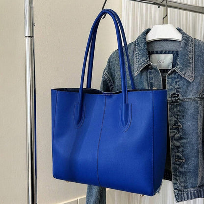 Blue minimalist shoulder tote bag made of PU leather with double handles, displayed with a denim jacket.