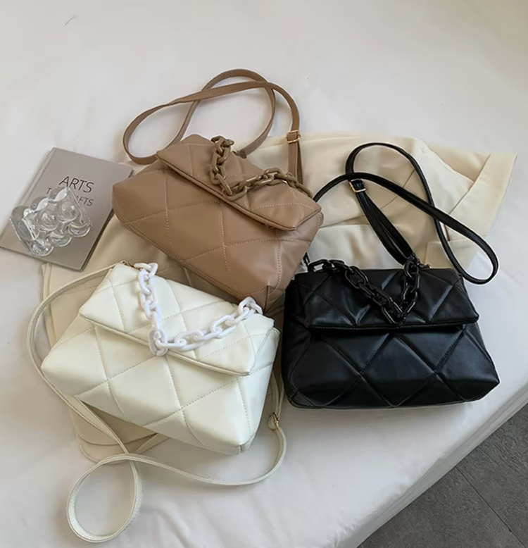 Three quilted handbags in beige, black, and white with chunky chain details on a light surface