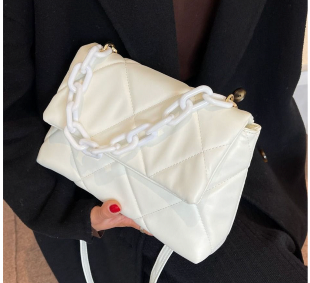 Beige quilted handbag with chunky white chain strap, held by person wearing black outfit.