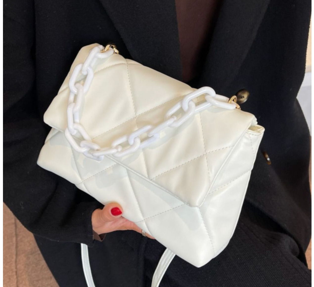 Beige quilted handbag with chunky white chain strap, held by person wearing black outfit.