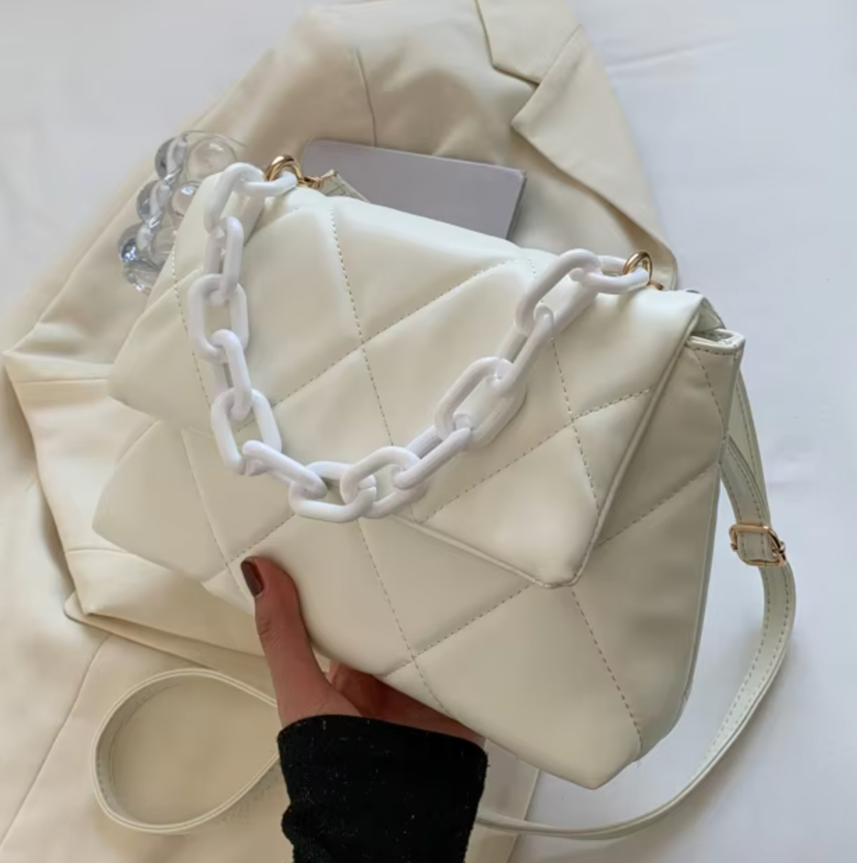 White fluffy quilted handbag with chunky plastic chain and adjustable shoulder strap on beige fabric background.