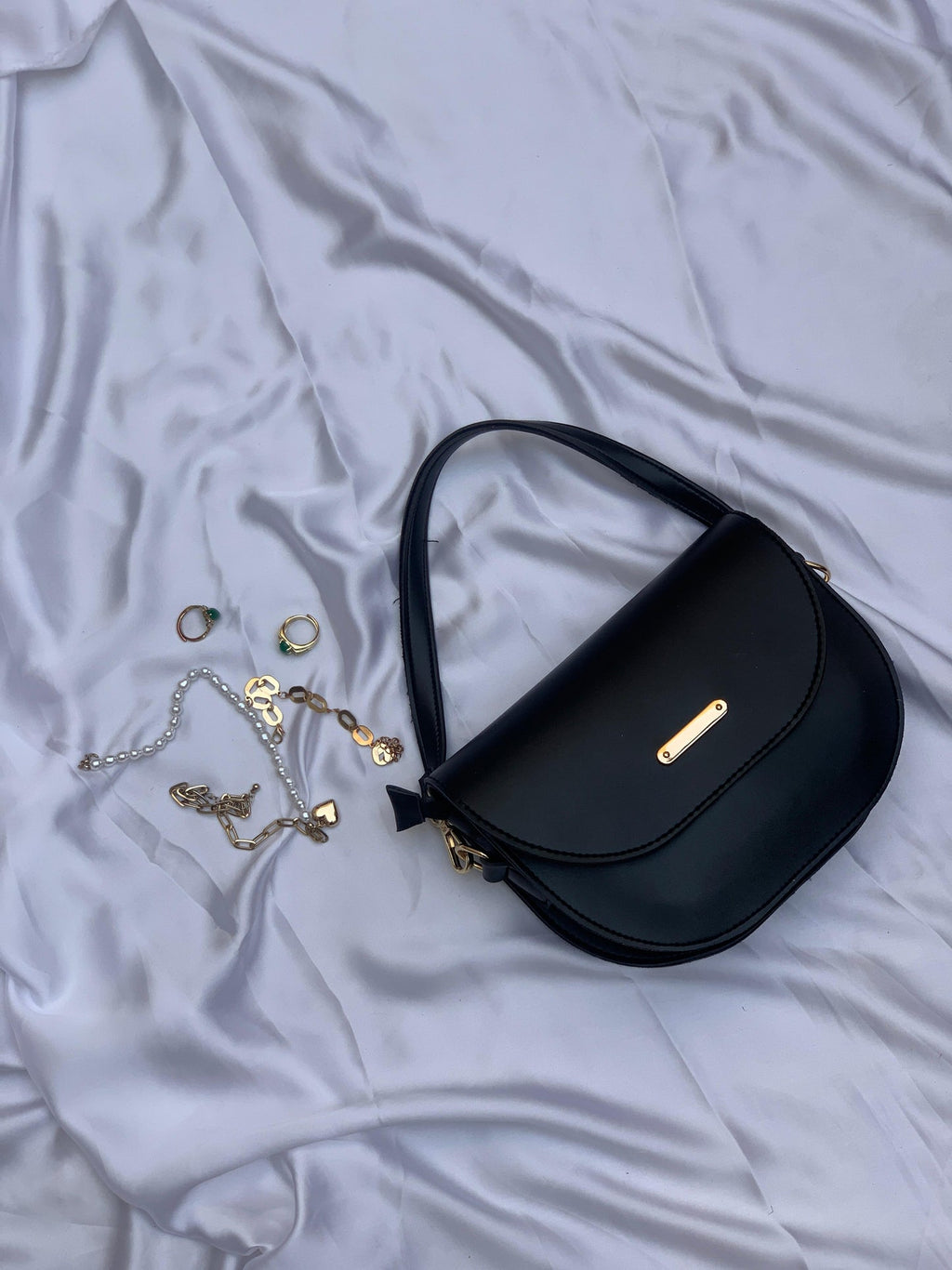 Elegant black dual strap bag with gold accents placed on silky fabric alongside gold jewelry pieces