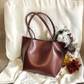 Brown faux leather tote bag with double handles styled with decorative flowers on fabric backdrop