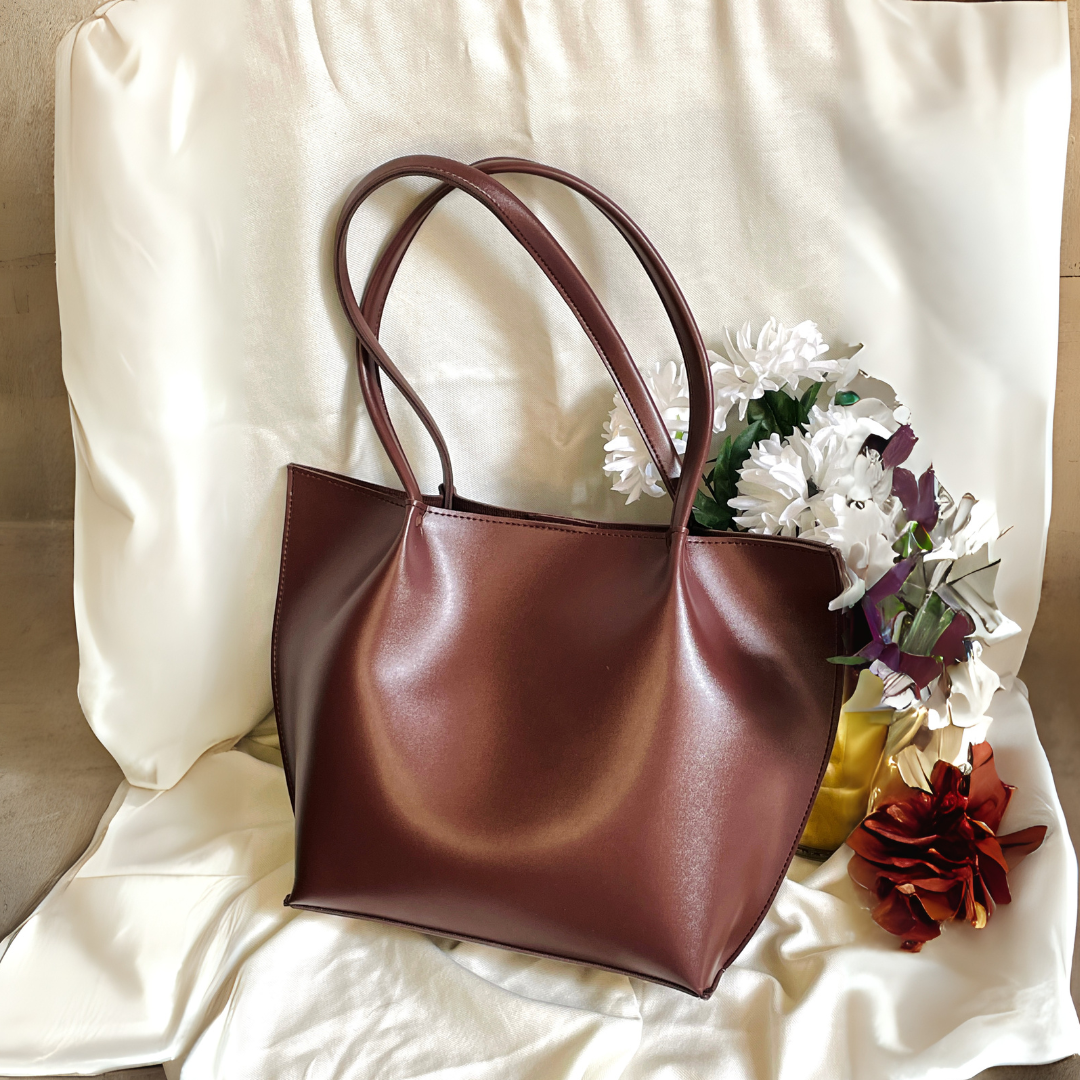 Brown faux leather tote bag with double handles styled with decorative flowers on fabric backdrop