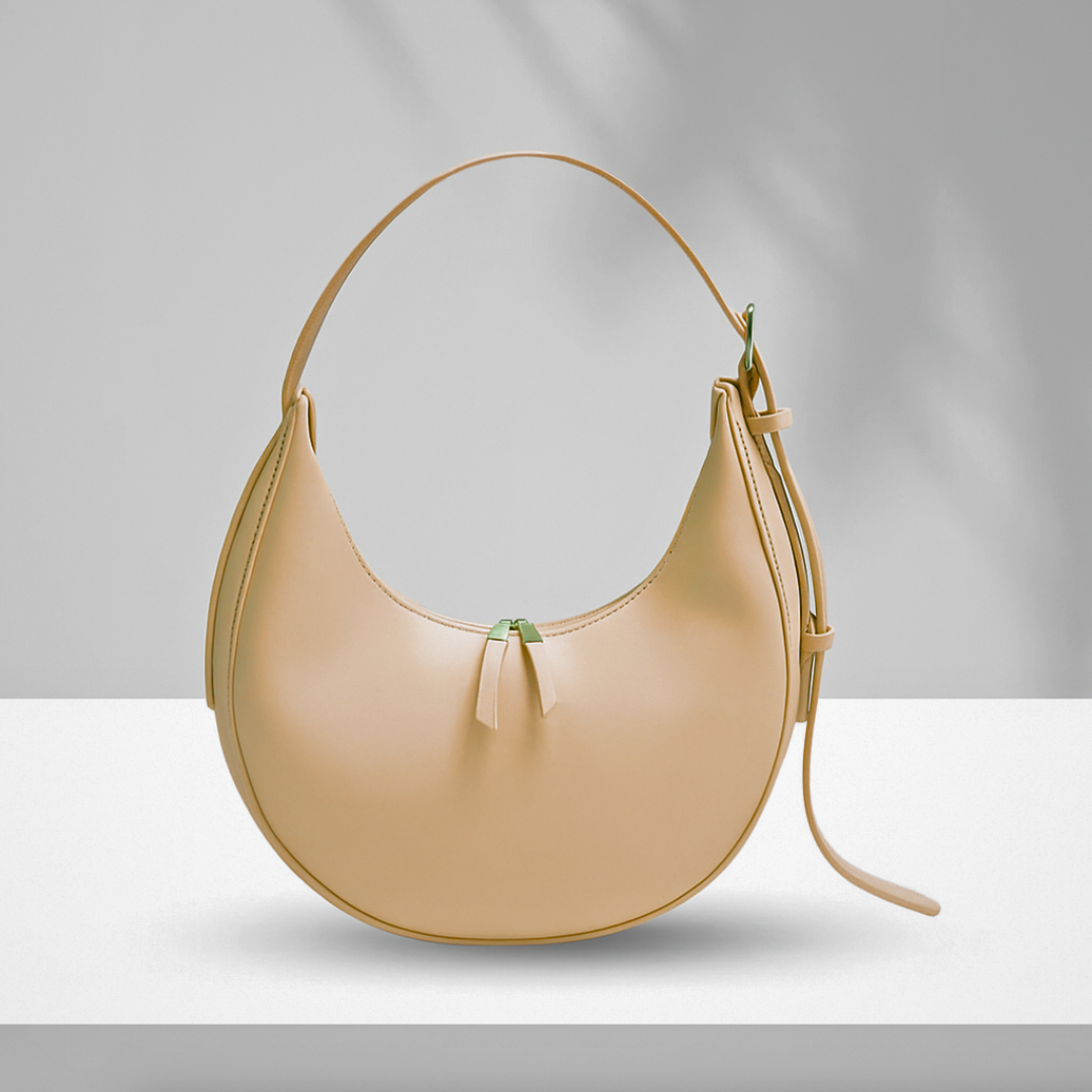 Beige U-shaped synthetic leather bag with single zipper and adjustable shoulder strap displayed on white surface